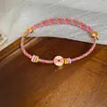 Close-up macro view of handwoven colorful cord bracelet with pink enamel lucky gold charm - Red/Pink