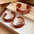 Dettaglio macro di tre bracciali rigidi in acrilico marmorizzato ambra in un portagioie - Marrone