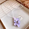 Vista dettagliata di un ciondolo a fiore in resina viola su una collana di cuoio bianco. - Viola