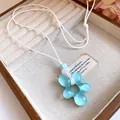 Primo piano di un ciondolo a fiore in resina azzurra su collana in pelle bianca - Blu