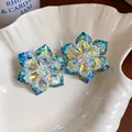 Makrodetailansicht schillernder Glasblumen-Ohrstecker in einer weißen Muschelschale - Weiß und Blau