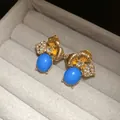 Macro view of vintage gold leaf stud earrings with blue oval stone and rhinestones - Gold-Blue
