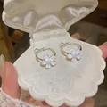 Close-up of elegant silver hoop earrings with white resin flowers in a shell box. - Silver-White