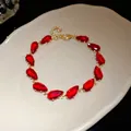 Elegant gold-tone bracelet with vibrant red teardrop-shaped zircon stones on a white tray - Bracelet - Gold / Red