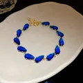 Elegant gold bracelet featuring blue teardrop-shaped zircon stones on a white plate - Bracelet - Gold / Dark Blue