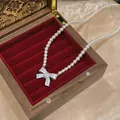 Detailed view of a bow pearl necklace displayed in a luxury red velvet jewelry box. - Silver-White
