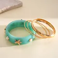 Close-up of a 4-piece teal resin and golden metal bangle set with starfish and faux pearls - Gold-Blue