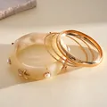 Close-up of bohemian resin starfish bangle and gold bracelets set with pearl accents - Gold-White