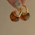 Dettaglio di orecchini a cerchio dorati a forma di C con pendenti in resina ambra traslucida. - Stile Giunzione Dorata a Forma di C (HE34154) / Marrone