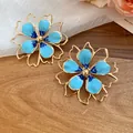 Close-up of blue enamel hollow flower stud earrings on a wooden background - Silver Post Stud Earrings (HE32038) / Blue