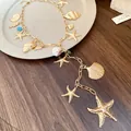Detailed close-up of a gold starfish and shell charm necklace for a beach vacation look. - Gold
