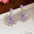 Dettaglio ravvicinato di orecchini a fiore in rafia viola e metallo dorato su scatola crema - Stile con perno dell'orecchino in argento / Oro con Viola