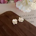 Detail view of flower-shaped zirconia clip-on earrings with white enamel petals - Gold Floral Style (HE32734)