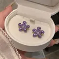 Macro detail of elegant purple zircon flower stud earrings displayed in white jewelry box - Flower Style / Purple