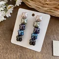 Macro detail of pearlescent flower drop earrings showing gradient pearly colors on white card - Gradient Coffee Green Blue