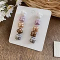 Close-up of five pairs of pearlescent flower stud earrings in varied colors on a white display card - Muted Colors