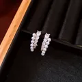 Primer plano detallado de elegantes pendientes curvos con circonitas y perlas blancas - Oro-Blanco