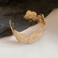 Detailed macro view of a gold metal open cuff bracelet featuring floral butterfly wing designs. - Gold (5#)