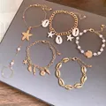 Conjunto de pulseras bohemias doradas con conchas, estrellas de mar y perlas sobre gris. - Juego de 5 Piezas (HB6060) / Oro-Blanco