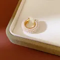Detalle macro de un elegante ear cuff dorado en forma de C con microperlas dobles - Clip de oreja único / Oro-Blanco
