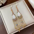 Macro view of 14K gold plated gourd tassel earrings featuring elegant white jade-like stones - Gourd Tassel Style / Gold