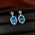 Close-up of elegant sparkling oval blue zircon drop earrings with halo stones on a black display - Earrings / Blue
