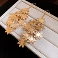 Dettaglio di eleganti orecchini pendenti a nappa con fiori in metallo dorato. - Oro