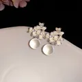 Gros plan détaillé de boucles d'oreilles fleurs en émail avec perles translucides brillantes - Beige