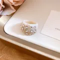 Detailed close-up of a cream resin ring with sparkling clear stone inlays on a gold tray - Ring / Ivory