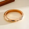 Macro view of chunky gold-toned hinged bangle with smooth mirror polished finish - Gold