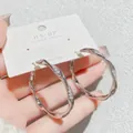Elegante silberfarbene Creolen mit Mikropavé-Verzierung auf weißer Schmuckkarte - Wellenförmiger Creolen-Stil / Ein Paar / Silber