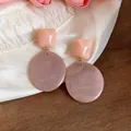 Dettaglio di orecchini pendenti geometrici in resina rosa e marmo su seta bianca - Viola