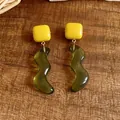 Dettaglio di orecchini a perno in resina quadrati gialli e ondulati verdi su legno. - Giallo-Verde