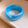 Gros plan d'un large bracelet en résine bleue translucide posé sur un livre ancien. - Bleu