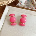 Gros plan de boucles d'oreilles en résine rose en forme de C avec un bord doré. - Rose