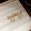 Macro view of gold-plated bow stud earrings with sparkling zircons and delicate pearls - Gold