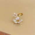 Dettaglio macro di un anello placcato oro con eleganti petali di fiori in smalto bianco - Aperto Regolabile / Oro-Beige