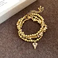 Dettaglio del set collana e bracciale con perline dorate e ciondolo a cuore lucido - Bracciale / Oro