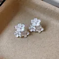Close-up of silver-tone floral stud earrings with white enamel finish on textured background. - Silver Needle Silver Style / White