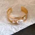 Detail view of a gold open cuff bracelet with three oval pearls and cutout design - Oval Hollow Pearl Bangle / Gold