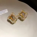 Macro view of gold stud earrings with orange square gem and sparkling stone halo. - Gold Brown