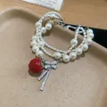 Detail view of a multi-layer pearl bracelet with a red apple and zircon bow charm. - White And Red