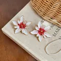 Macro detail of red and white enamel flower stud earrings placed on a vintage book surface. - Gold Style / White
