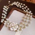 Detailed view of a multi-layer glass pearl necklace with a cream enamel flower pendant - Gold-White