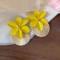 Primo piano di orecchini a fiore giallo smaltato con base circolare a pieghe dorate - Orecchini Tondi Fiore / Giallo