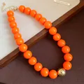 Close-up of vibrant orange chunky beads and gold sphere detail on fashion necklace. - Necklace / Orange
