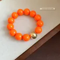 Close-up of bright orange large bead bracelet with one metallic gold spherical bead. - Bracelet / Orange