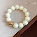 Close-up of oversized cream beads and a single gold bead on a minimalist bracelet - Bracelet / Beige