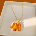 Close-up of a bohemian orange resin elephant pendant on a delicate gold chain necklace - Elephant Pendant Necklace (HN12577) / Amber