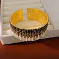 Primo piano di un elegante bracciale rigido multistrato con strass sfumati oro. - Sfumatura Grigio Nero Oro